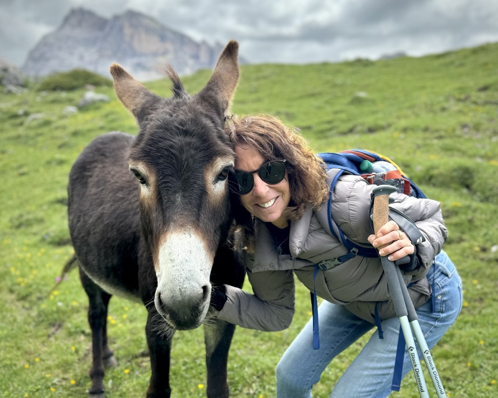 Sherri Wolff smiling with her cheek against a donkey in a green mountain meadow