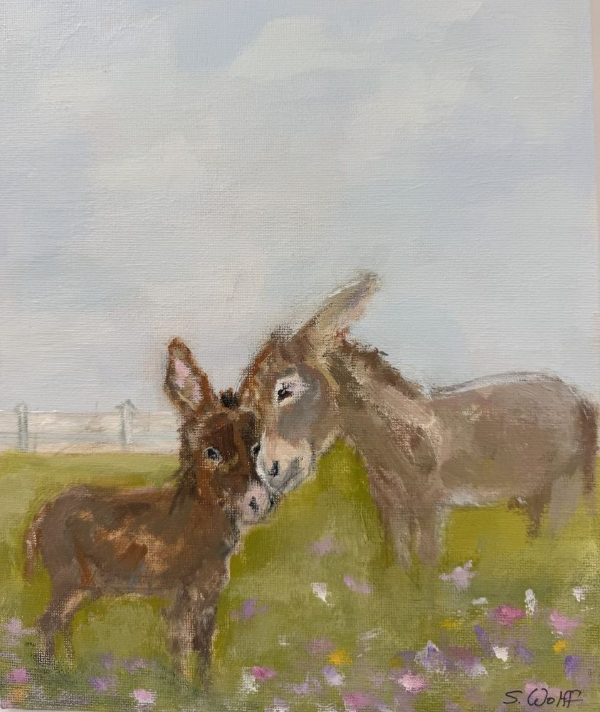 A baby donkey nuzzling its mother in a field of wildflowers