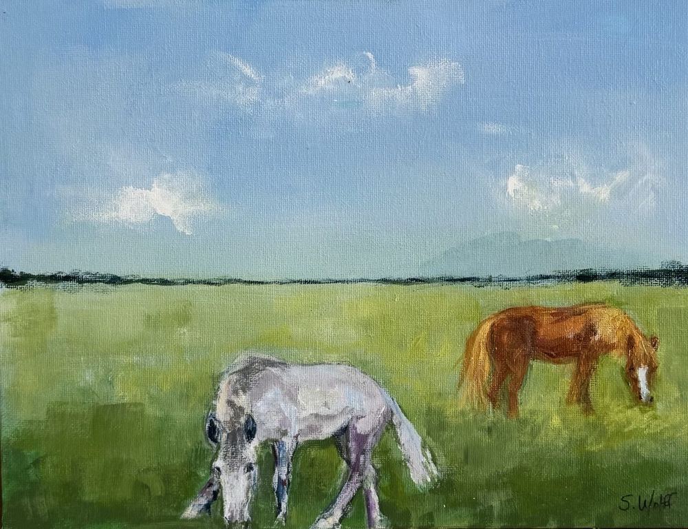 A white horse and a chestnut horse grazing in a green pasture